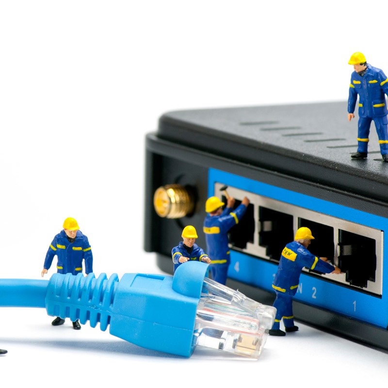IT Solutions section - Team of miniature it technicians plugging in an Ethernet cable to into a switch.