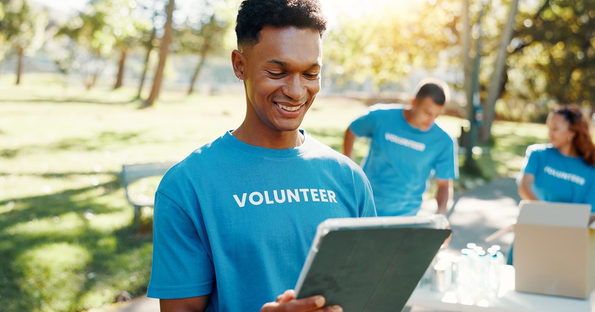Volunteer using a tablet outdoors with team in background.